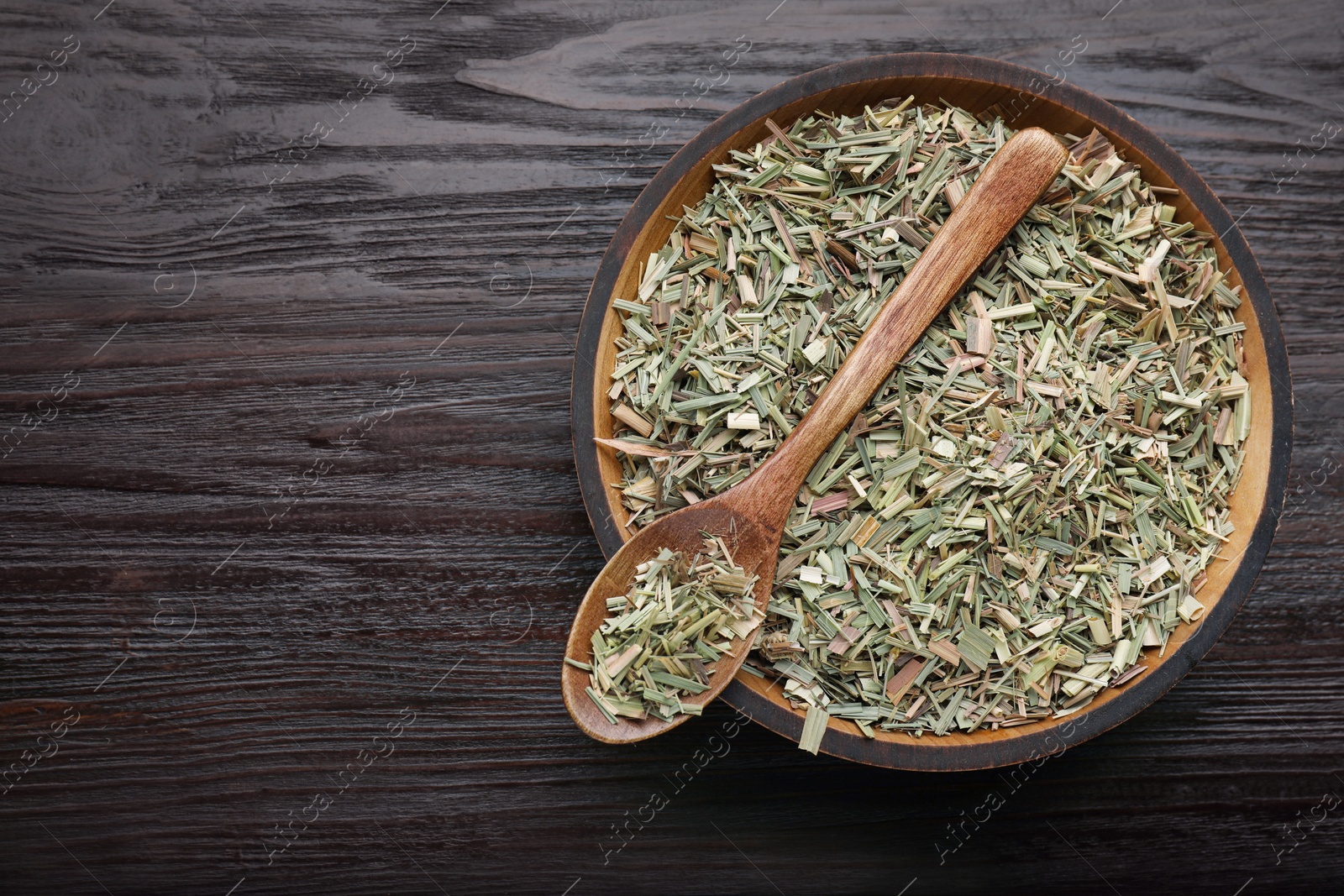 Photo of Bowl with aromatic dried lemongrass and spoon on wooden table, top view. Space for text