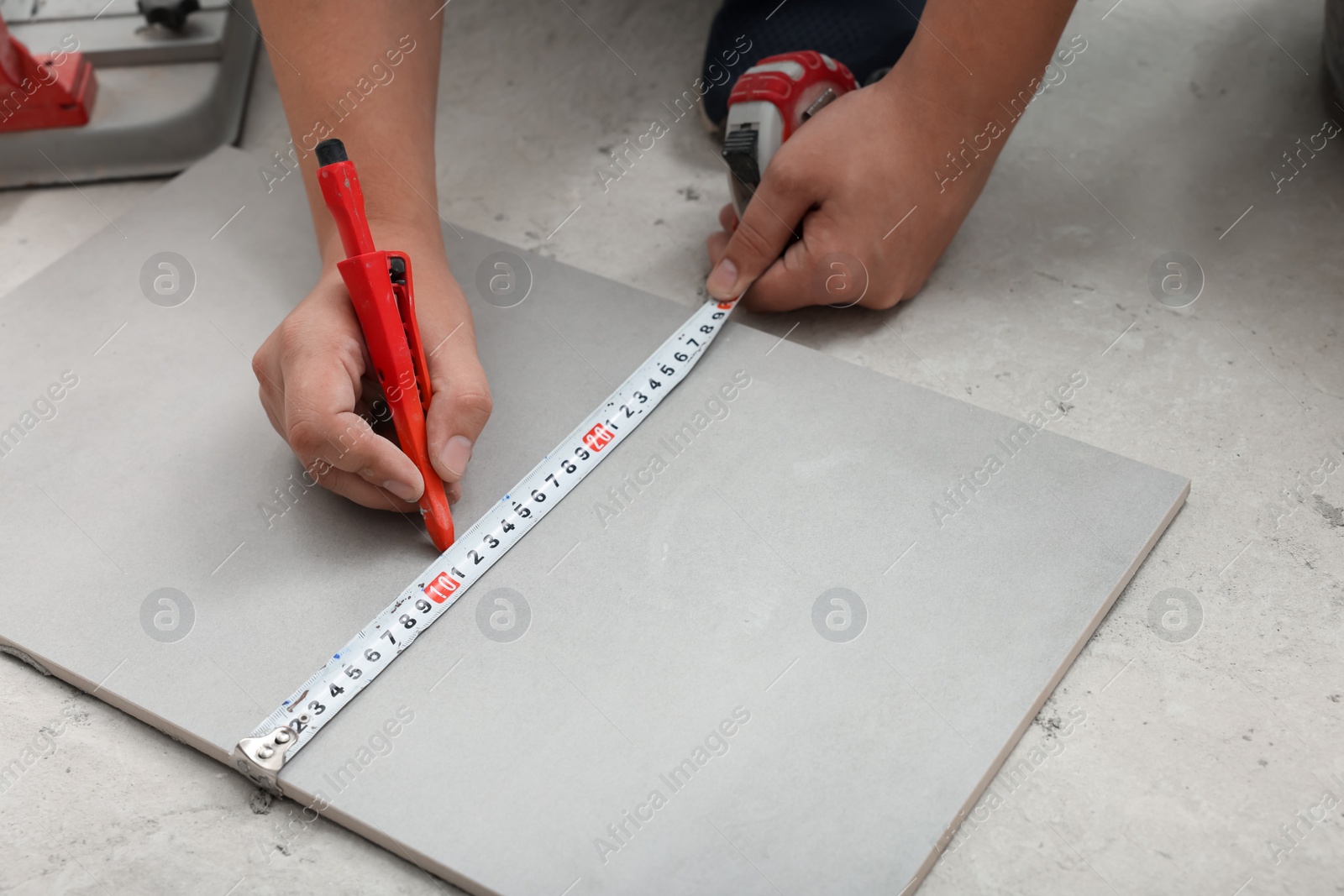 Photo of Worker measuring and marking ceramic tile on floor, closeup