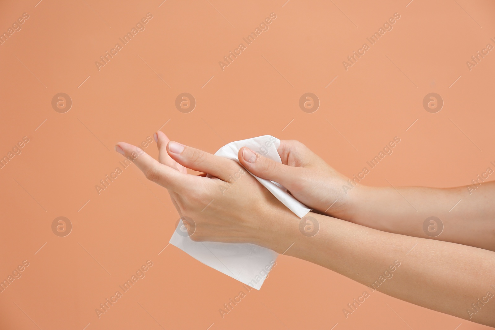 Photo of Woman cleaning hands with paper tissue on light brown background, closeup