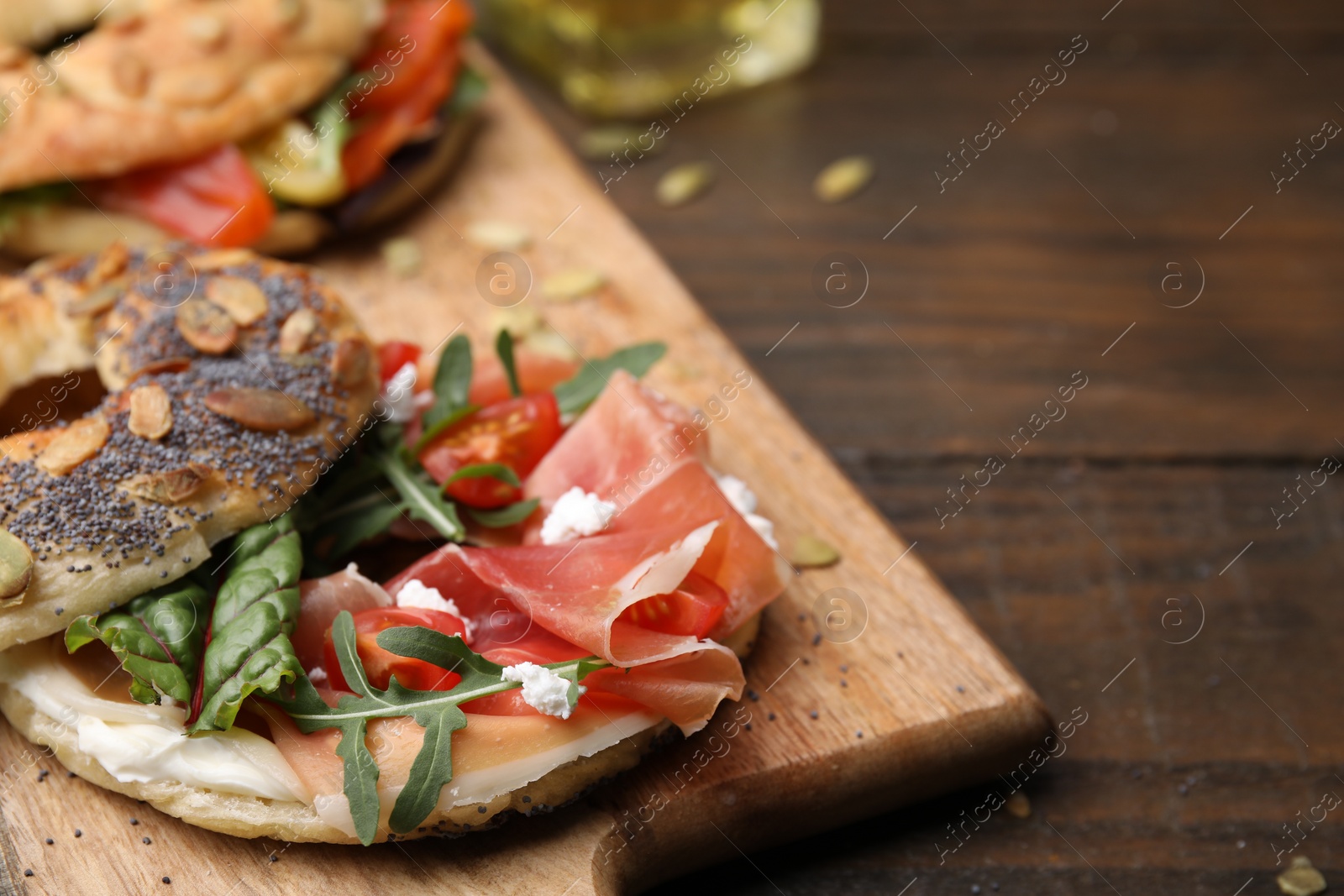 Photo of Tasty bagel with cured ham, cream cheese, tomatoes and arugula on wooden table, closeup. Space for text