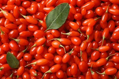 Photo of Fresh ripe goji berries with leaves as background, top view