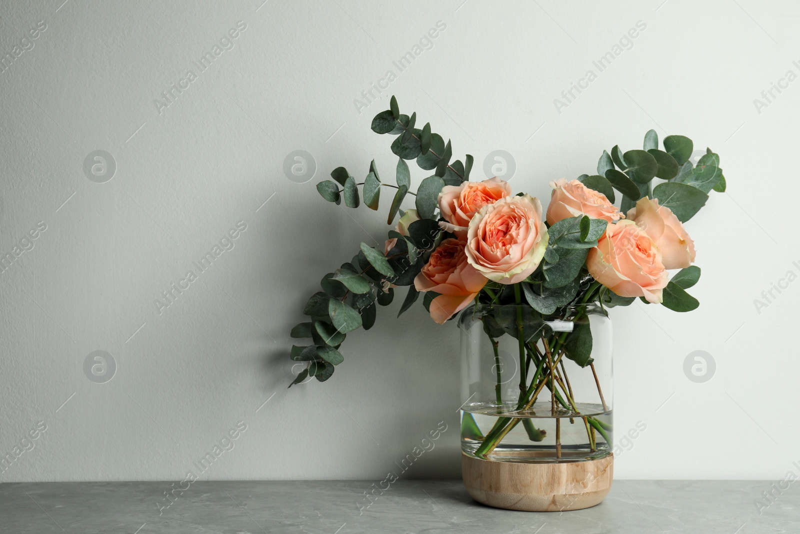 Photo of Bouquet of beautiful flowers in glass vase on grey table against white background. Space for text