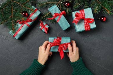 Photo of Woman holding Christmas gift box with red bow at dark grey table, top view