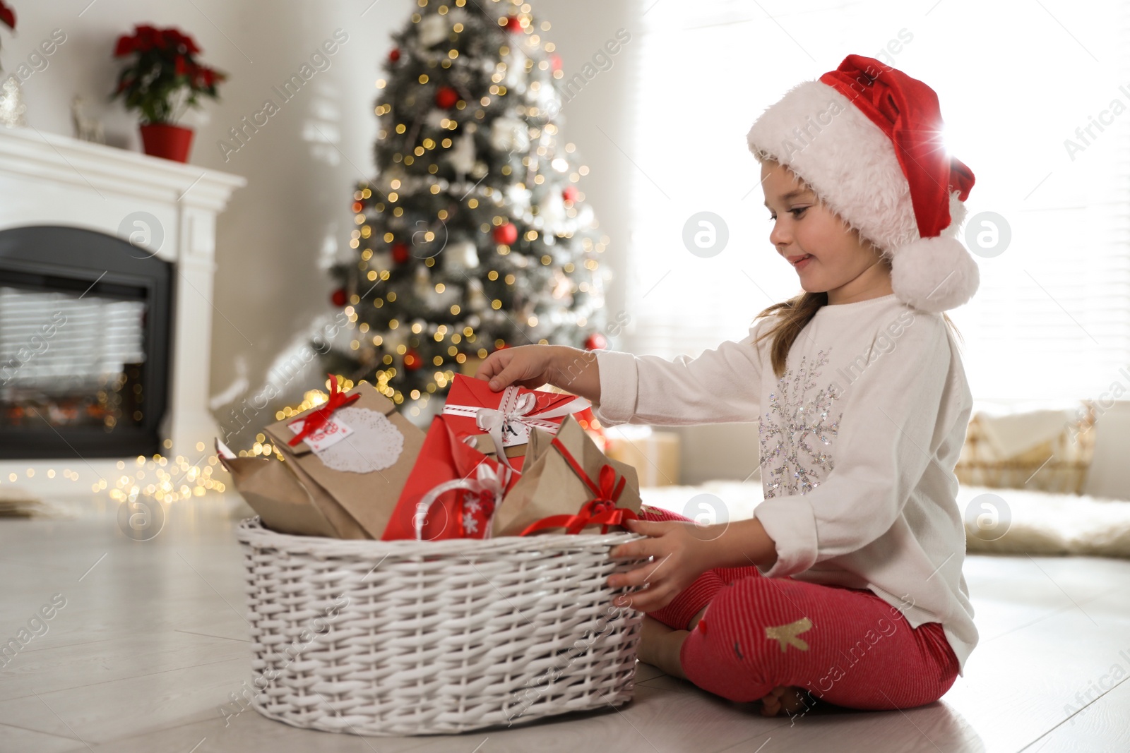 Photo of Cute little girl in Santa hat taking gift from Christmas advent calendar at home