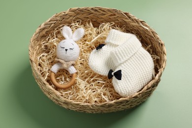 Photo of Different baby accessories in wicker box on green background, above view