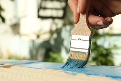 Photo of Woman painting wooden surface with blue dye outdoors, closeup. Space for text