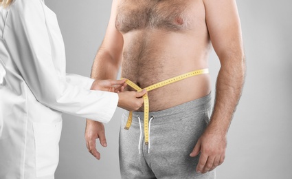 Photo of Doctor measuring man's waist on grey background, closeup. Weight loss