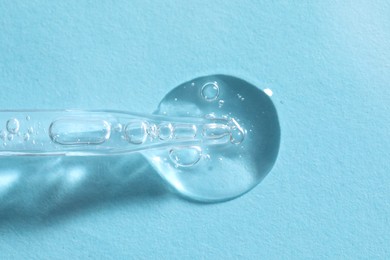 Photo of Glass pipette and transparent liquid on light blue background, top view