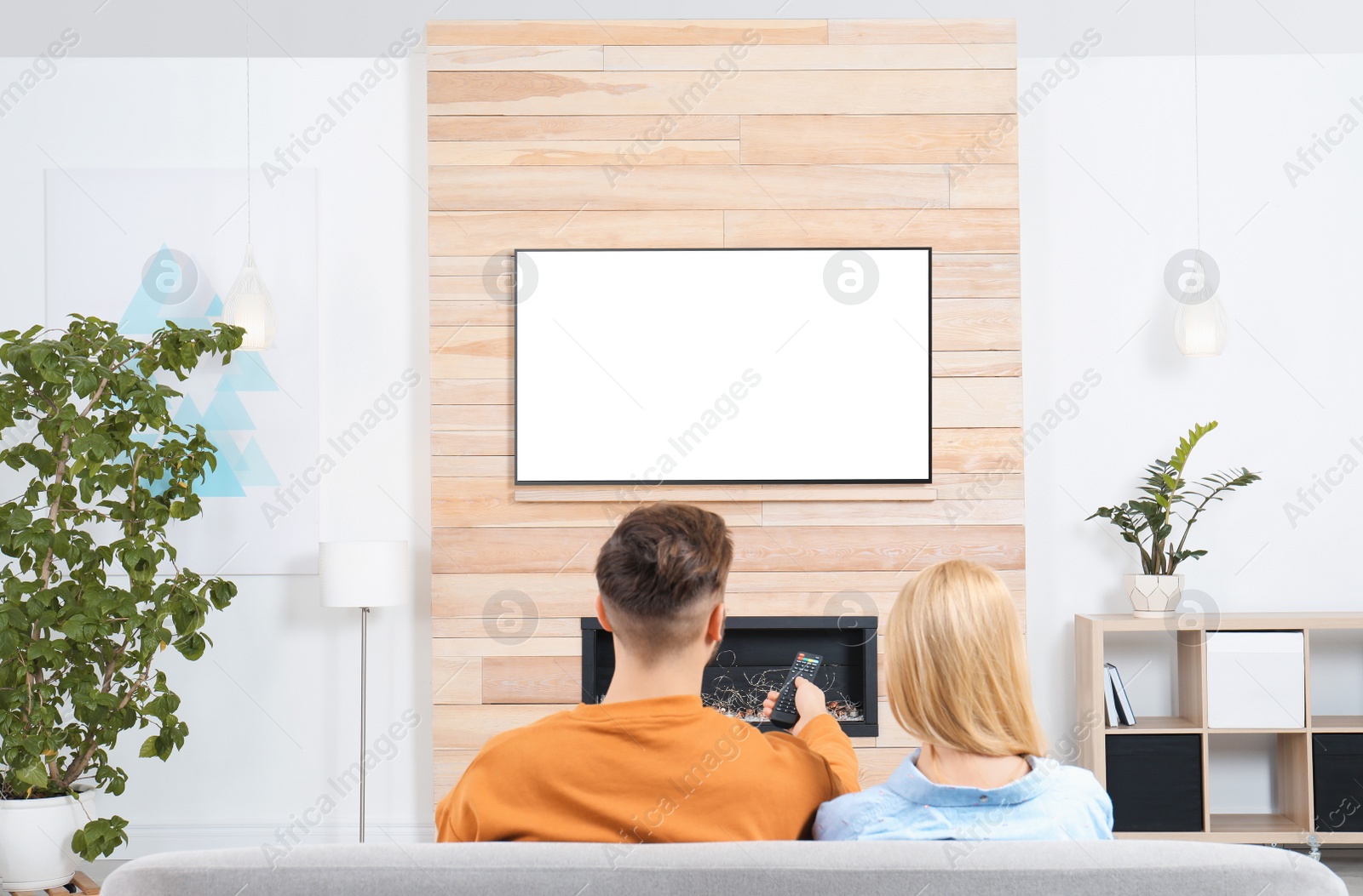 Photo of Couple watching TV on sofa in living room with decorative fireplace