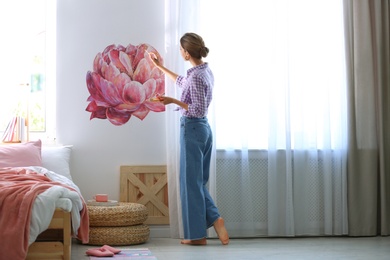 Photo of Young interior designer painting flower on wall in modern room
