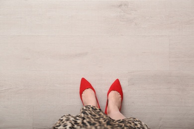 Photo of Woman in red shoes standing on wooden floor, top view. Space for text