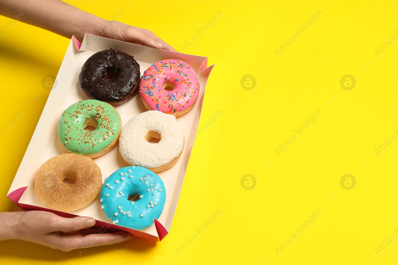 Photo of Woman with box of delicious donuts on yellow background, closeup. Space for text