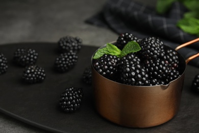 Metal saucepan with tasty blackberries on grey table