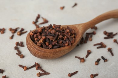 Photo of Aromatic dry cloves and wooden spoon on white table, closeup