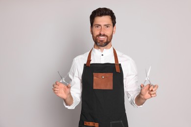 Photo of Smiling hairdresser wearing apron holding scissors on light grey background