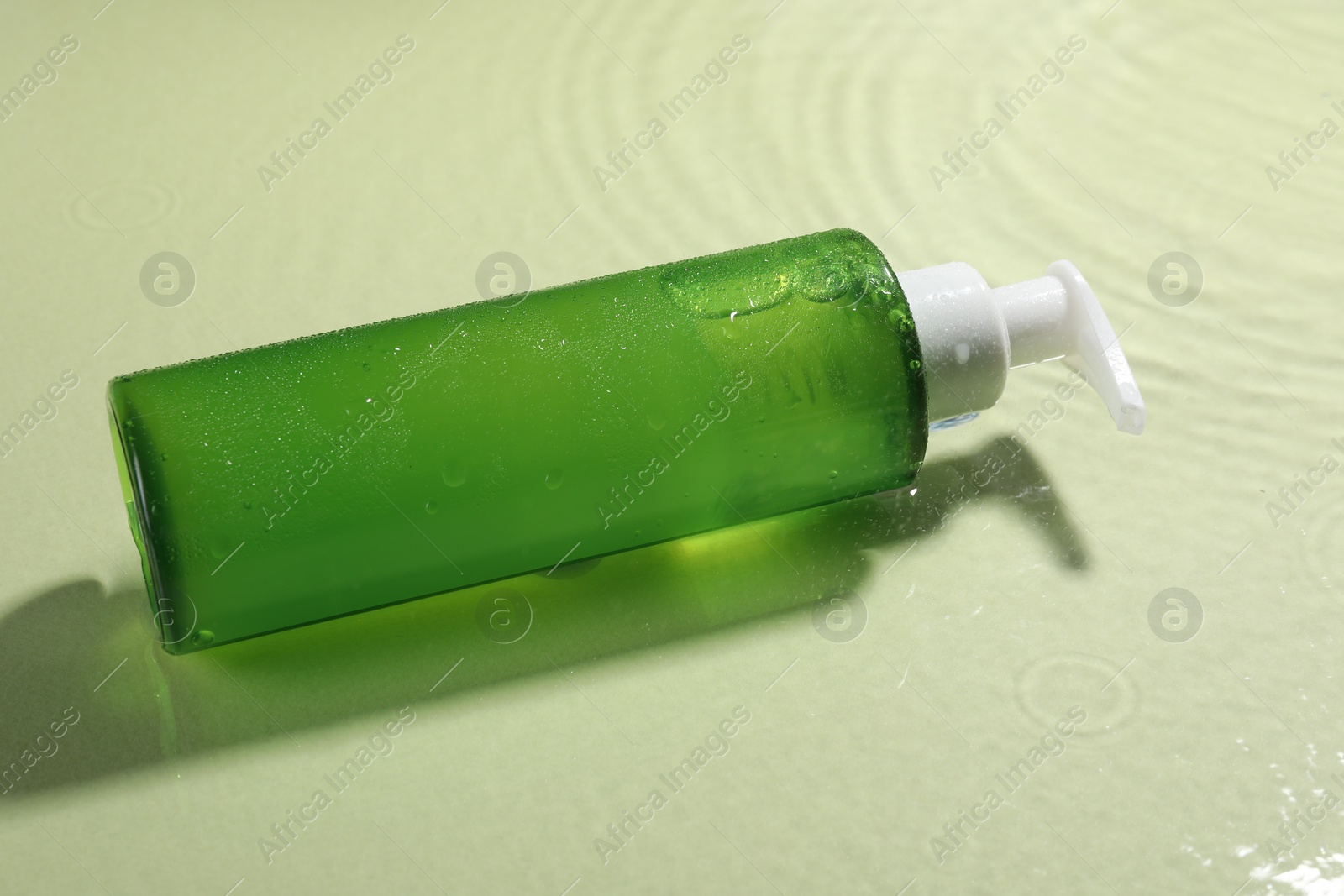 Photo of Bottle of facial cleanser in water against olive background