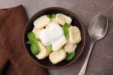 Photo of Bowl of tasty lazy dumplings with sour cream and mint leaves on brown table, flat lay