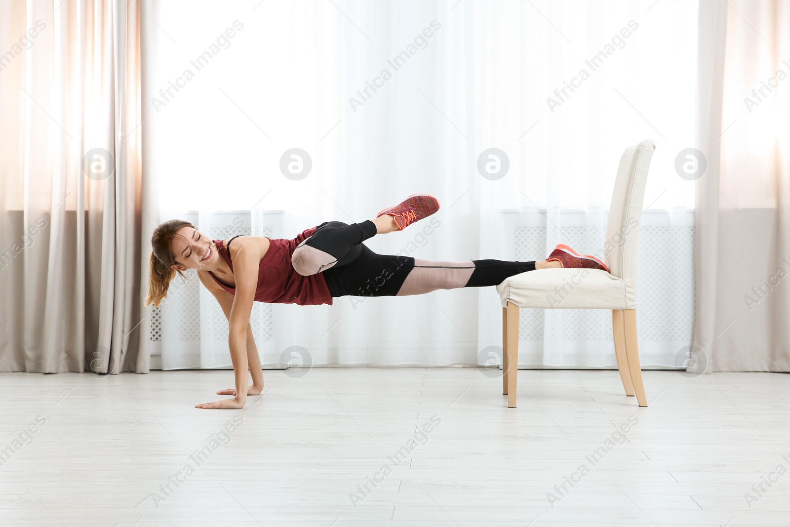 Photo of Young woman exercising with chair indoors. Home fitness