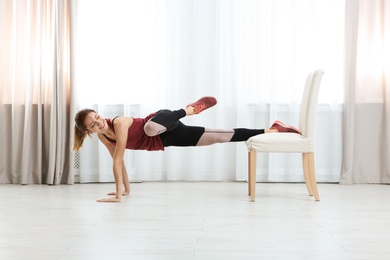 Photo of Young woman exercising with chair indoors. Home fitness