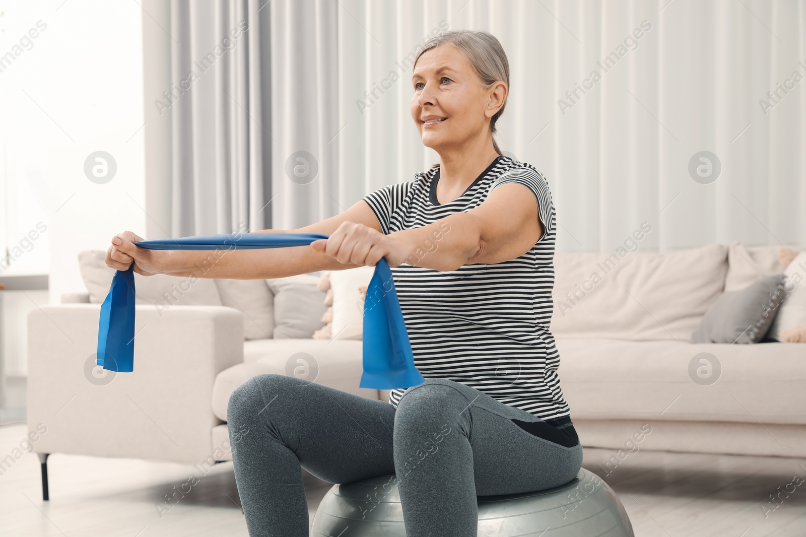 Photo of Senior woman doing exercise with elastic resistance band on fitness ball at home