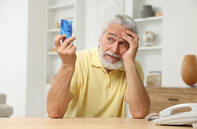 Photo of Confused senior man with credit card at home. Be careful - fraud