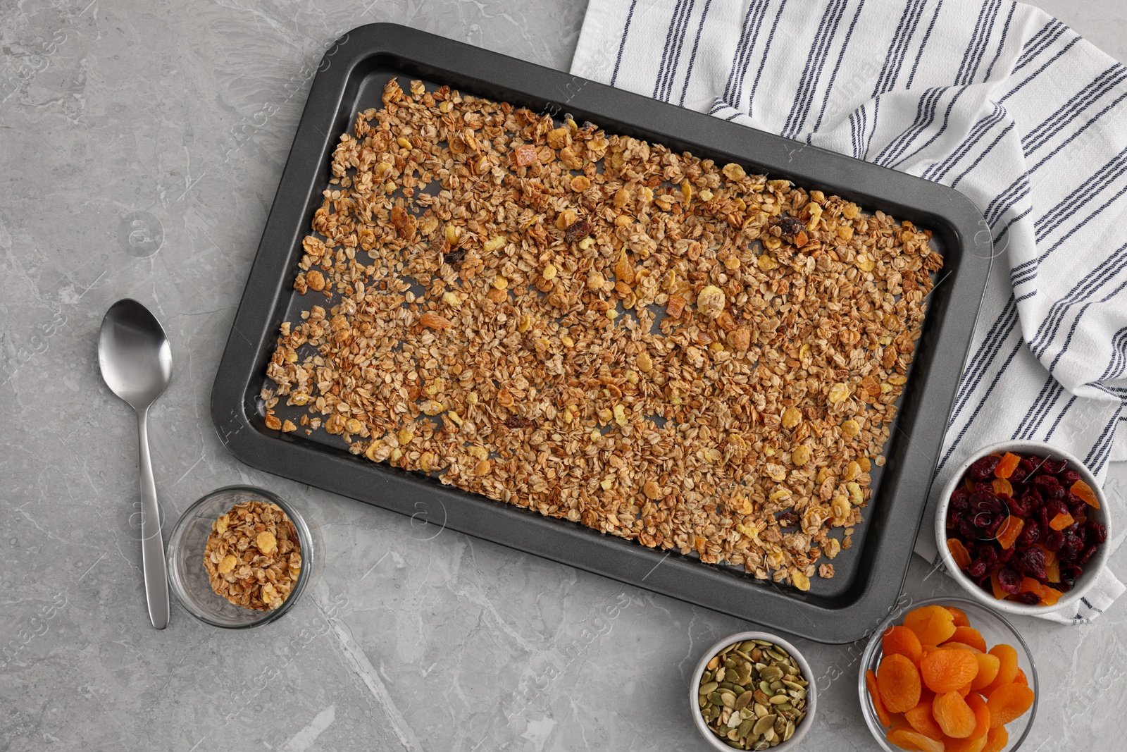 Photo of Making granola. Baking tray with mixture of oat flakes and other ingredients on grey marble table, flat lay