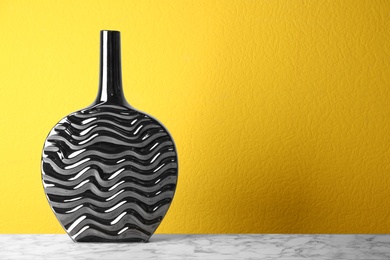 Photo of Stylish black ceramic vase on white marble table against yellow background. Space for text