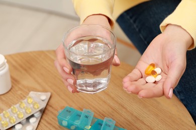 Photo of Woman holding glass of water and pills indoors, closeup