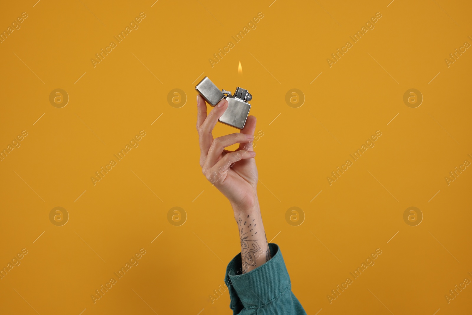 Photo of Woman holding lighter with burning flame on orange background, closeup