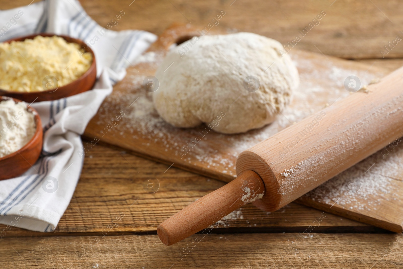 Photo of Rolling pin, flour and dough on wooden table, closeup