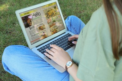 Woman reading online magazine on laptop outdoors, closeup