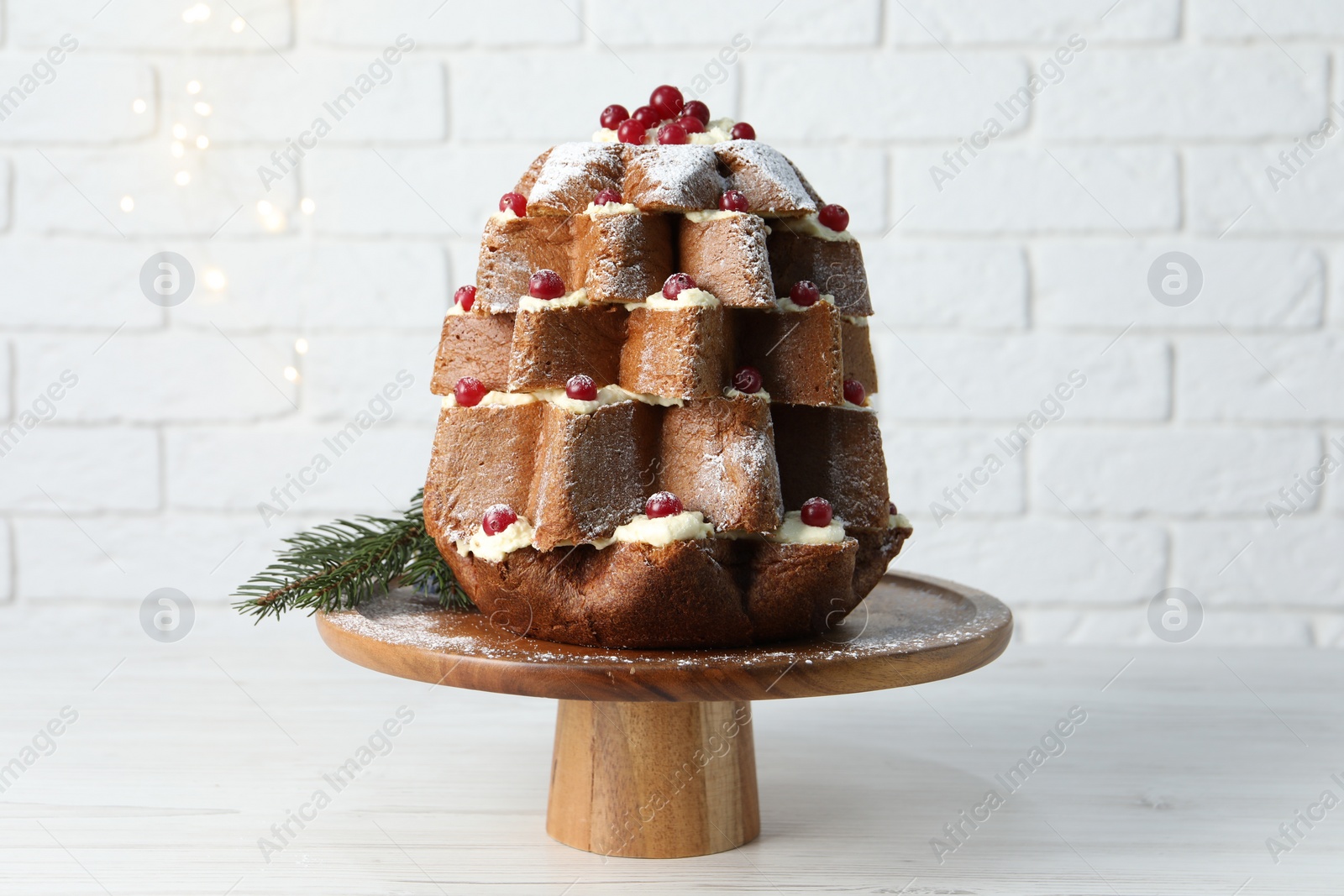 Photo of Delicious Pandoro Christmas tree cake with powdered sugar and berries on white table near brick wall