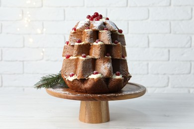 Delicious Pandoro Christmas tree cake with powdered sugar and berries on white table near brick wall