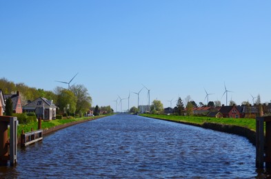 Photo of Beautiful small town with canal and wind turbines on sunny day. Alternative energy source