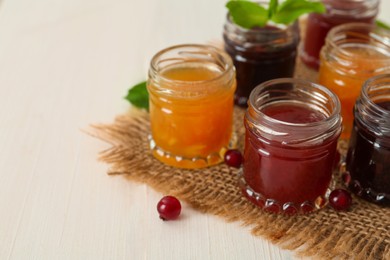 Jars of different jams on white table, space for text