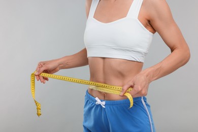 Photo of Slim woman measuring waist with tape on grey background, closeup. Weight loss