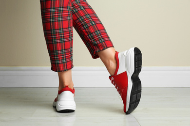 Woman wearing stylish sneakers near beige wall indoors, closeup