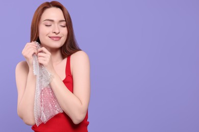 Photo of Woman popping bubble wrap on purple background, space for text. Stress relief