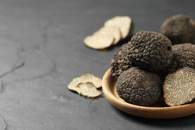 Photo of Black truffles in wooden plate on grey table. Space for text