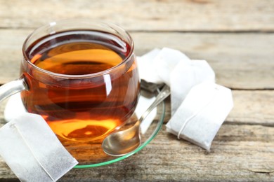 Photo of Aromatic tea in glass cup, spoon and teabags on wooden table