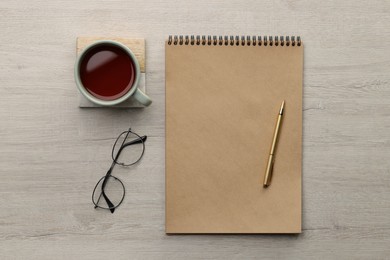 Photo of Ballpoint pen, notebook and cup of tea on wooden table, flat lay