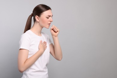 Photo of Young woman coughing on light grey background, space for text. Sore throat