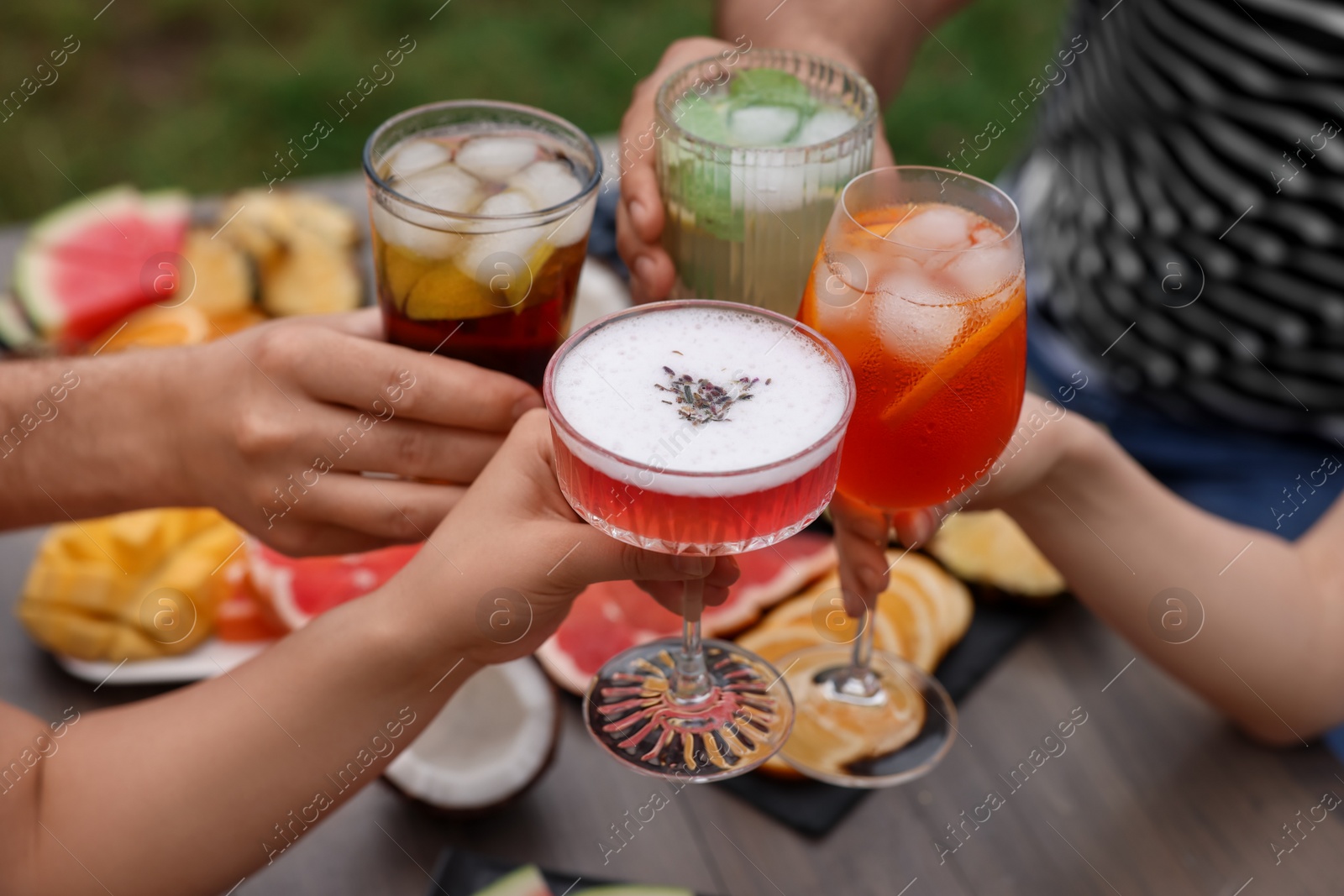 Photo of Friends clinking glasses with cocktails at table outdoors, closeup