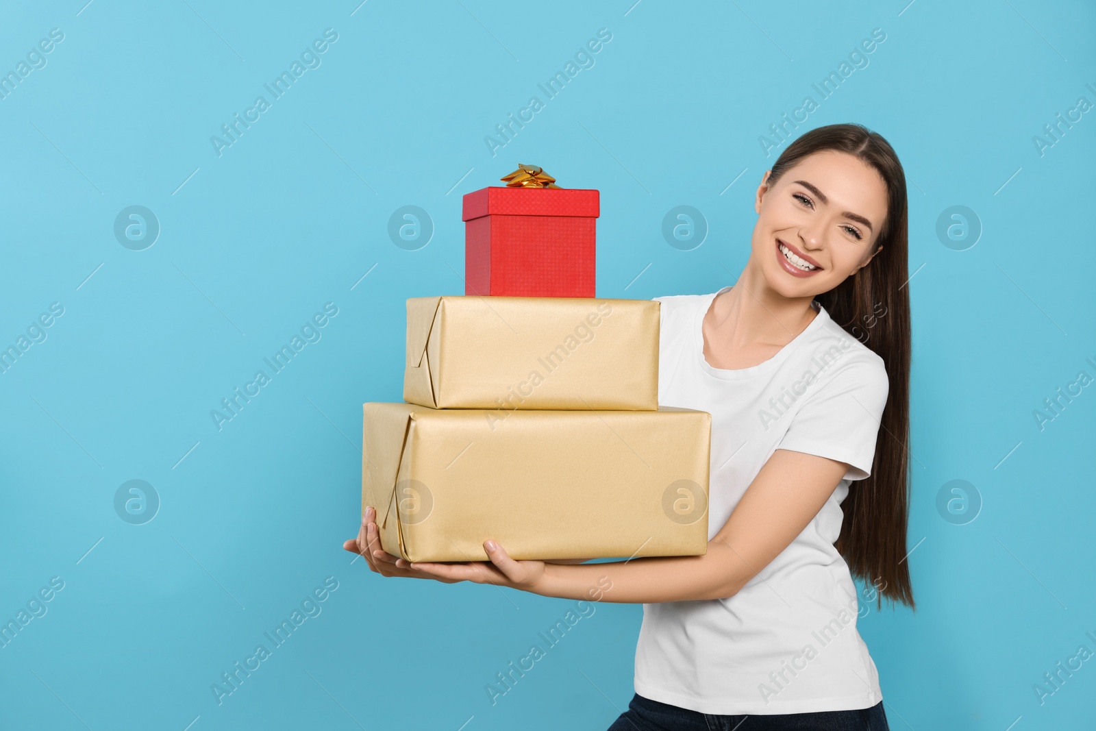 Photo of Portrait of happy young woman with gift boxes on light blue background