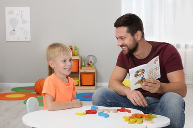 Photo of Motor skills development. Happy father helping his son to play with colorful wooden arcs at white table in room