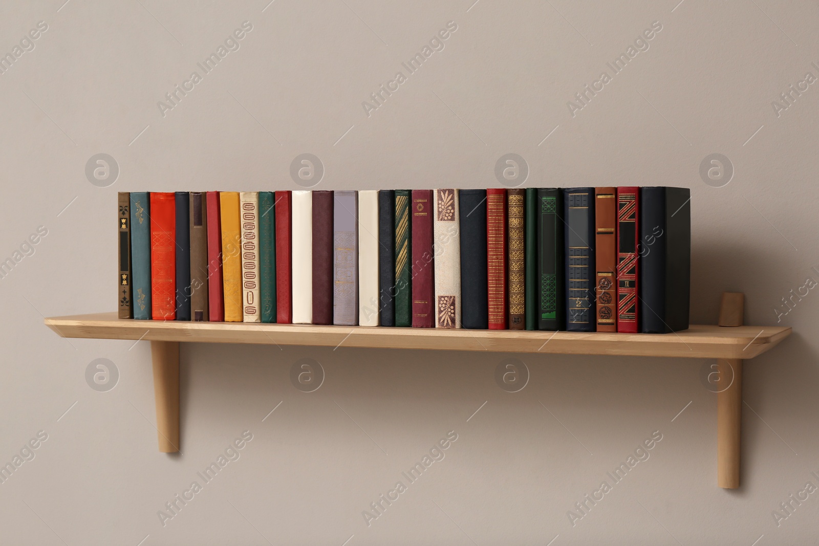 Photo of Wooden shelf with different books on light wall