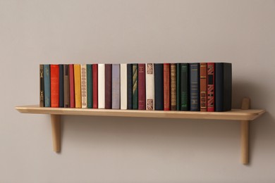 Wooden shelf with different books on light wall