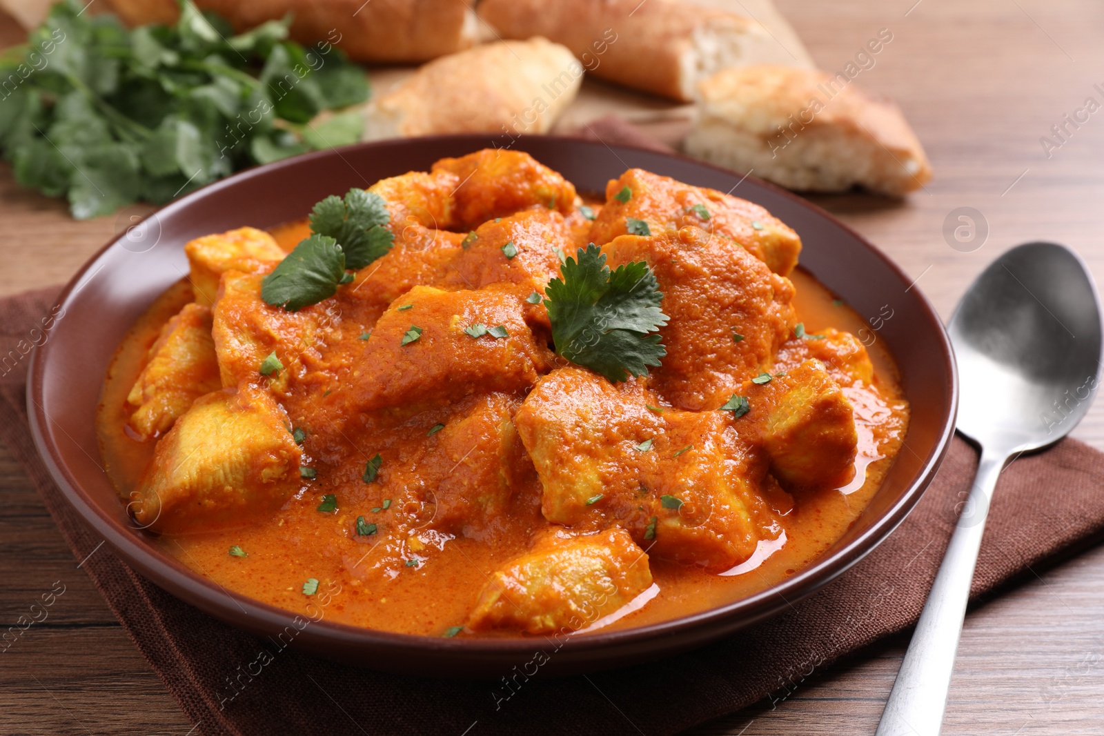 Photo of Bowl of delicious chicken curry on wooden table, closeup