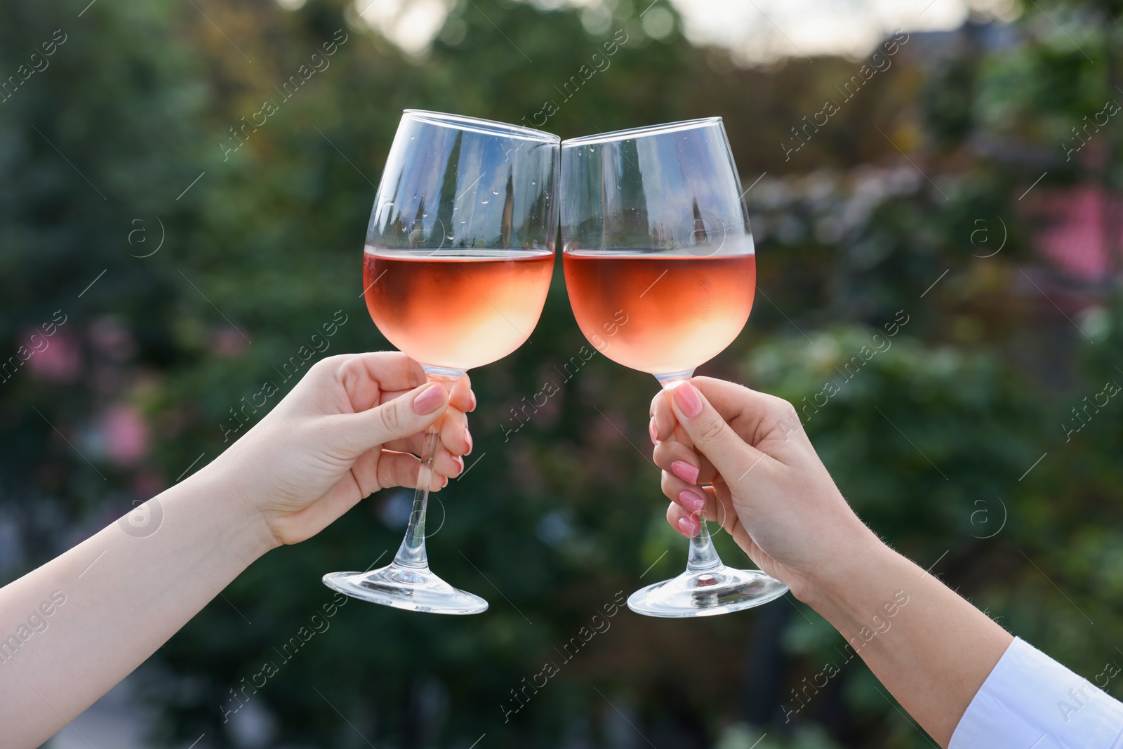 Photo of Women clinking glasses with rose wine outdoors, closeup