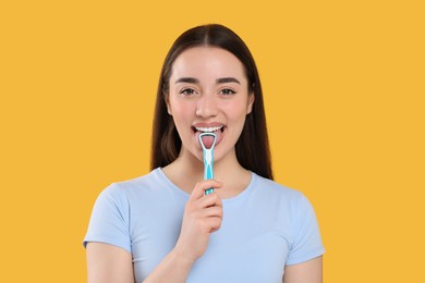 Photo of Happy woman brushing her tongue with cleaner on yellow background
